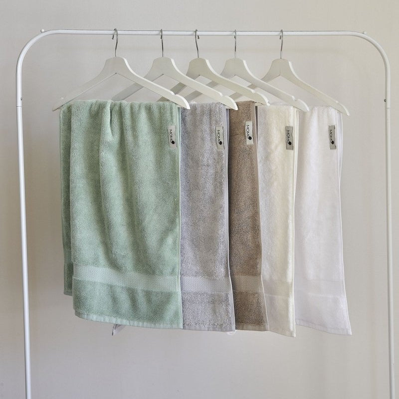 Five pastel bamboo towels displayed on white wooden hangers against neutral background, showing green, gray, brown, cream and