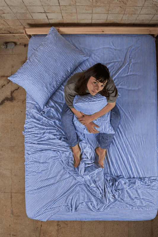 Mulher deitada na cama usando jogo de cama em algodão de bambu com listras azuis, vista de cima