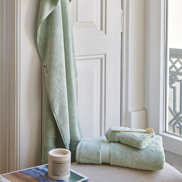 Mint green bamboo towel set by Alba displayed on windowsill with rolled towels and toothbrush