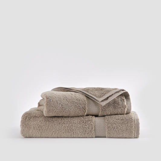 Beige bamboo towel set stacked, showing face cloth, hand towel, and bath towel against white background