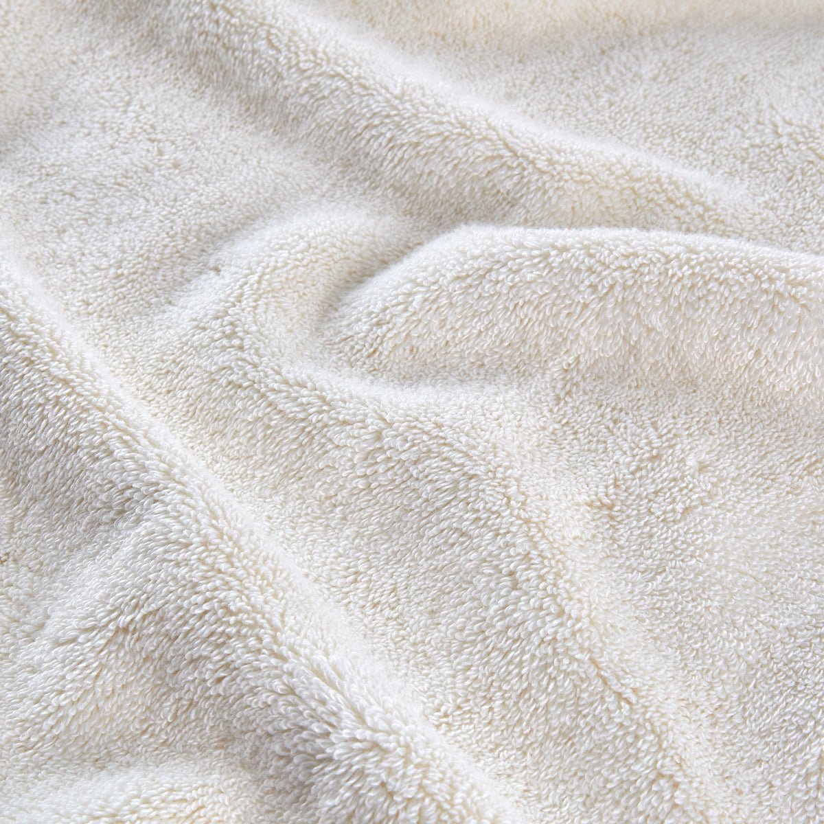 Cream-colored bamboo towel set folded and stacked, showing soft texture and natural fibers detail