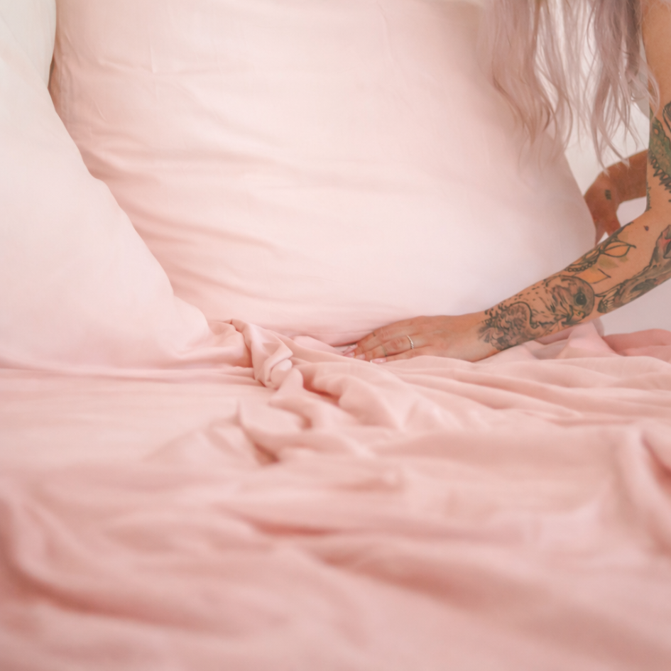 Close-up of a pink bamboo flat sheet being adjusted over the mattress, showing flexibility and softness.