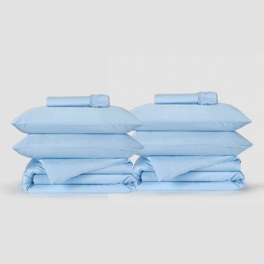Two light blue duvet cover sets from Momo Cotton neatly stacked with pillows and folded bedding displayed against a neutral b