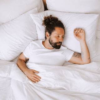 Man sleeping peacefully on a bed with white sheets, surrounded by minimalist and comfortable bedding conveying deep rest and well-being.