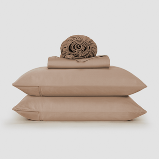 Beige bamboo sheet set stacked with rolled duvet cover and two pillows on white background