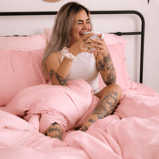 Woman lying comfortably on pink bamboo sheets, emphasizing the silky texture and soft draping.